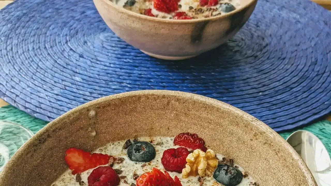 Anti-Inflammatory Two bowls of oatmeal topped with fresh strawberries, blueberries, raspberries, and a walnut piece are placed on a blue woven mat. \