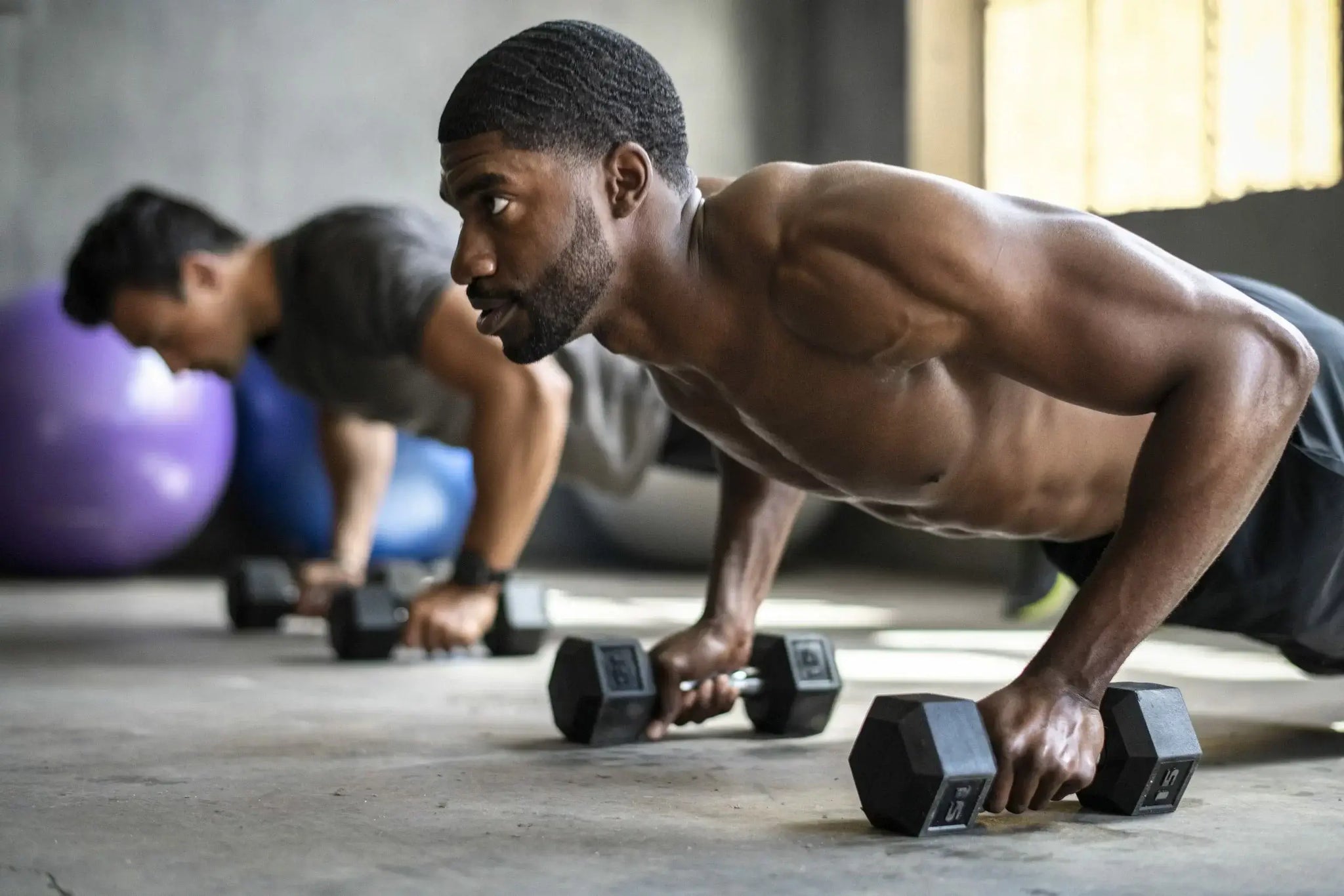 Two men are performing push-ups while gripping dumbbells in a gym. Should bodybuilders