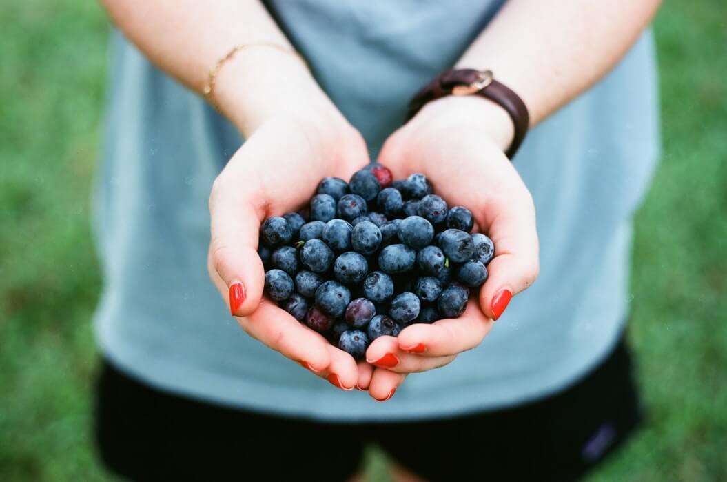 Person with painted nails holds a handful of blueberries, one of the best natural anti-aging foods.
