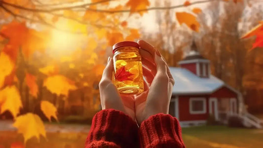 Hands in a red sweater hold a jar with a maple leaf inside, against a background of vibrant autumn leaves