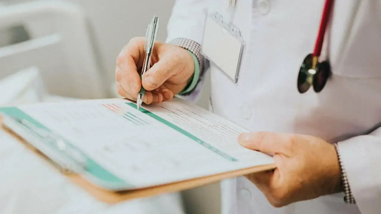 A medical professional wearing a white coat, identified by a stethoscope around their neck and an ID badge, is holding a clipboard.