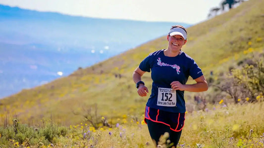 A person wearing a blue shirt, black shorts, and a white visor runs on a grassy hill with race number 152 on their chest,