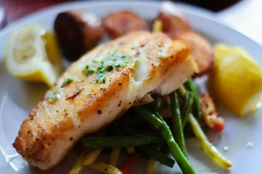 Plate of seared white fish garnished with chopped herbs, served over a bed of sautéed green beans and mixed vegetables.