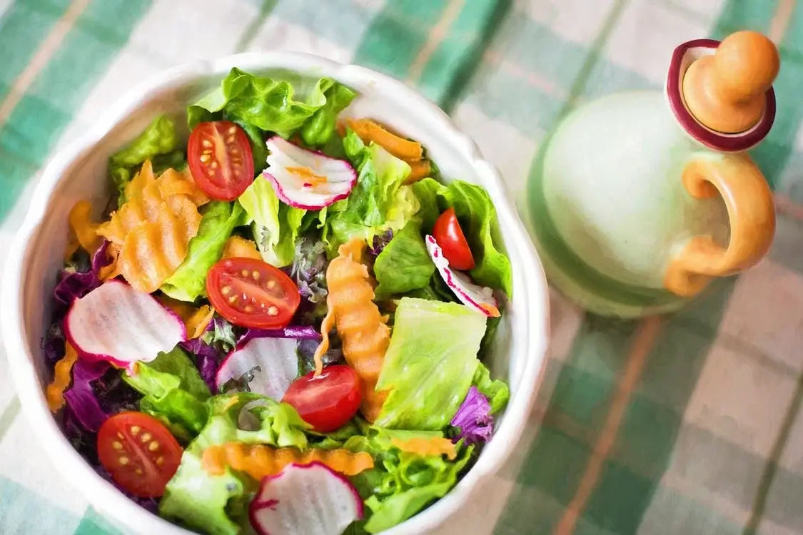 A fresh salad in a white bowl containing lettuce, cherry tomatoes, radish slices, and crinkle-cut carrot pieces.