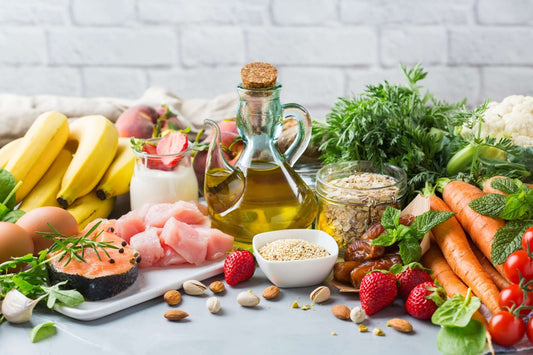 A colorful assortment of healthy foods on a table, including bananas, salmon, chicken, eggs, olive oil, yogurt with strawberries
