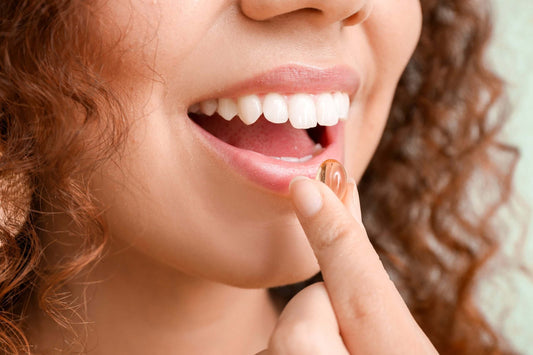 A close-up of a person with curly hair holding a gel capsule pill near their mouth.