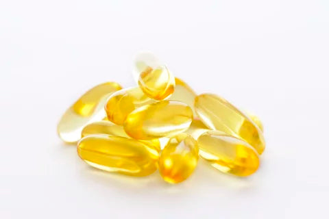A pile of yellow transparent gel capsules, infused with vitamin E oil, are scattered against a plain white background.