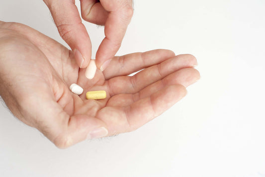Close-up of hands holding various pills, likely vitamins for joint pain relief, against a plain white background.