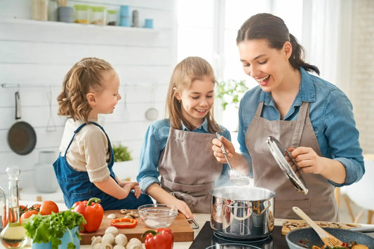 A woman and two children, all wearing aprons, are cooking together in a bright kitchen.