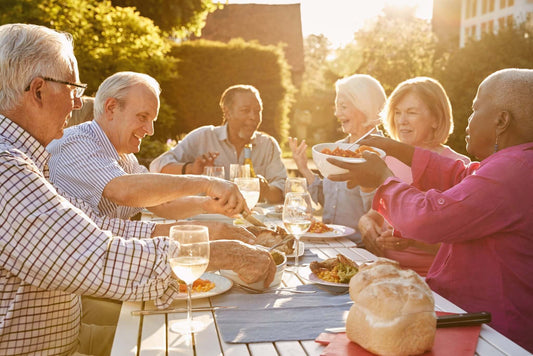 A group of older adults seated around an outdoor table, sharing a meal loaded with foods rich in Omega-3 fatty acids — an undercover love story for the liver.