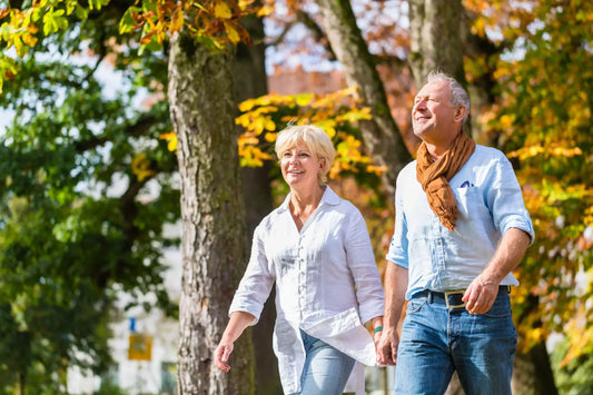 An older couple holding hands and walking in a park on a sunny day.