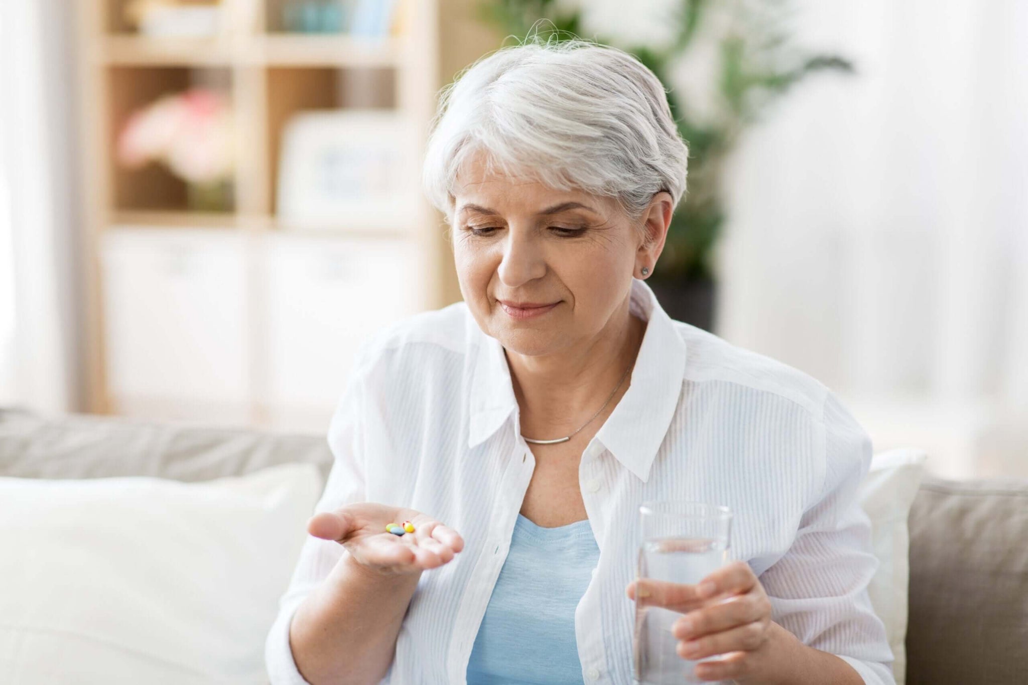 An older woman with short gray hair is sitting on a couch.
