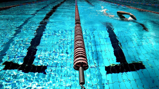 A swimmer wearing a cap and goggles swims in a lane at a clear blue pool.