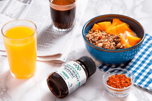 A breakfast table with a blue bowl of yogurt topped with granola and orange slices, a glass of orange juice