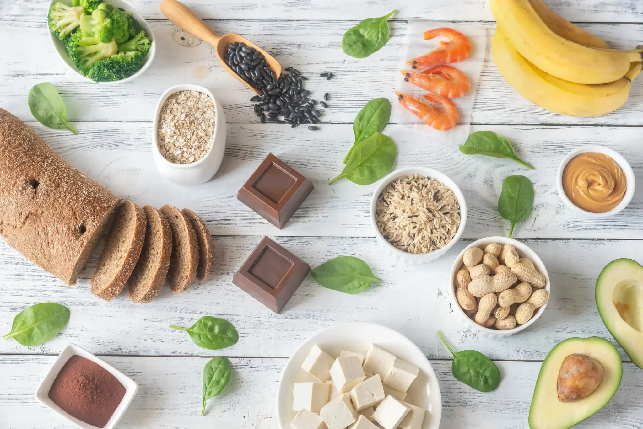 An assortment of magnesium-rich foods displayed on a wooden surface, including bread, broccoli, oats, black beans, shrimp