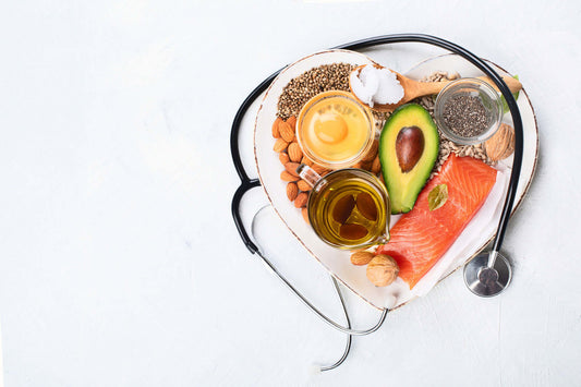 A heart-shaped dish containing various healthy foods including salmon, avocado, almonds, chia seeds, walnuts, olive oil, and an egg yolk.