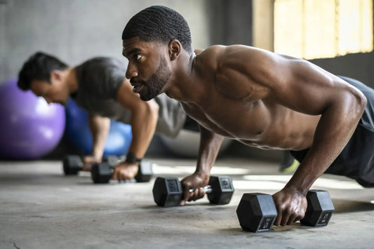 Two men are performing push-ups while gripping dumbbells in a gym.
