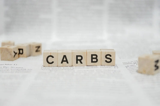 Scrabble tiles on a white surface spell out the word "CARBS." Carbohydrates