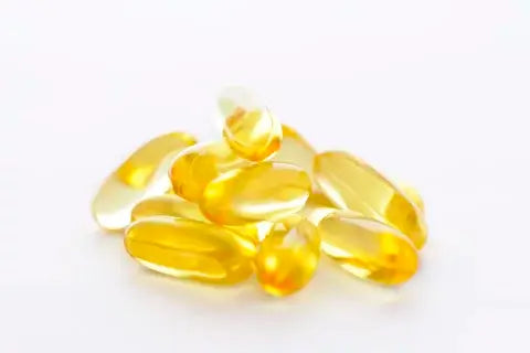 A pile of yellow transparent gel capsules, infused with vitamin E oil, are scattered against a plain white background.