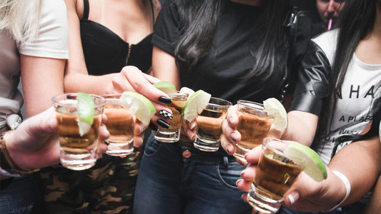 A group of people raising shot glasses filled with a golden liquid, likely alcohol, each garnished with a lime wedge.