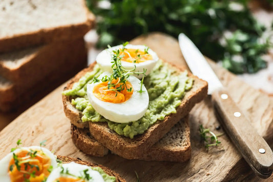 Slices of toast topped with mashed avocado, halved boiled eggs, and a sprinkle of fresh herbs.