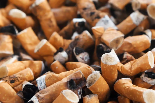 A close-up image of numerous used cigarette butts piled together, showing varying degrees of ash and scorch marks.