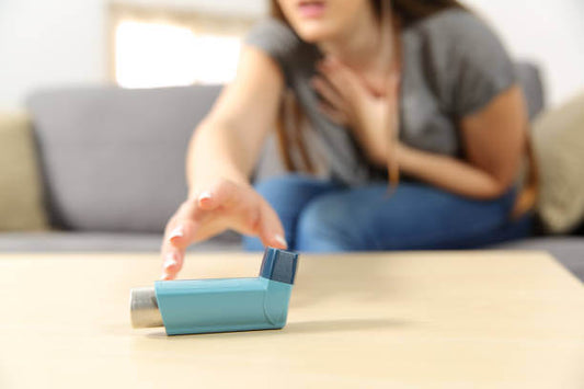 A person reaching for a blue asthma inhaler on a table while holding their chest, clearly in distress.