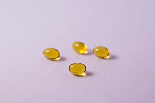 Four yellow, oval-shaped gel capsules are arranged on a light purple surface, hinting at 3