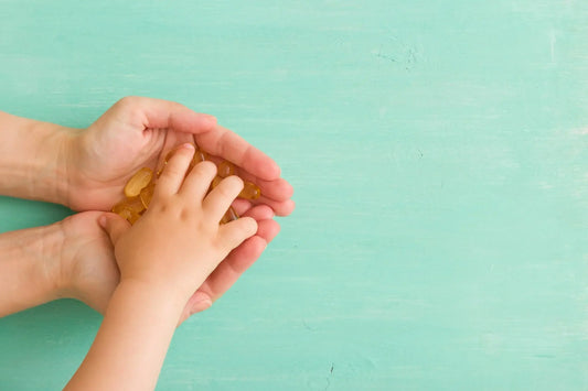 Adult hands holding a child's hand, both grasping a small pile of golden gummy vitamins