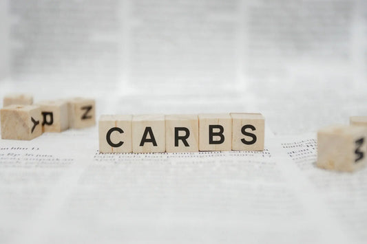 Scrabble tiles on a white surface spell out the word "CARBS."