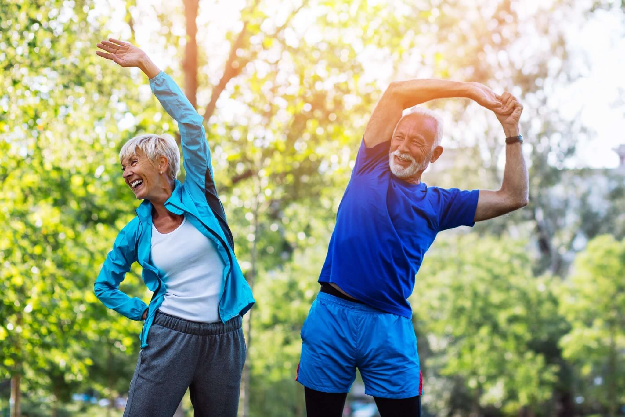 Two elderly individuals, one male and one female, are performing side stretches outdoors.