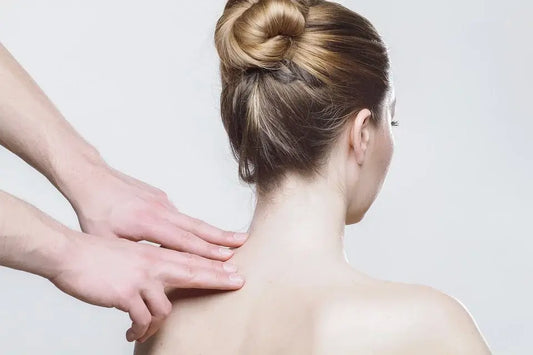 A person with blonde hair in a bun is receiving one of the best massages for arthritis on the upper back and neck from another