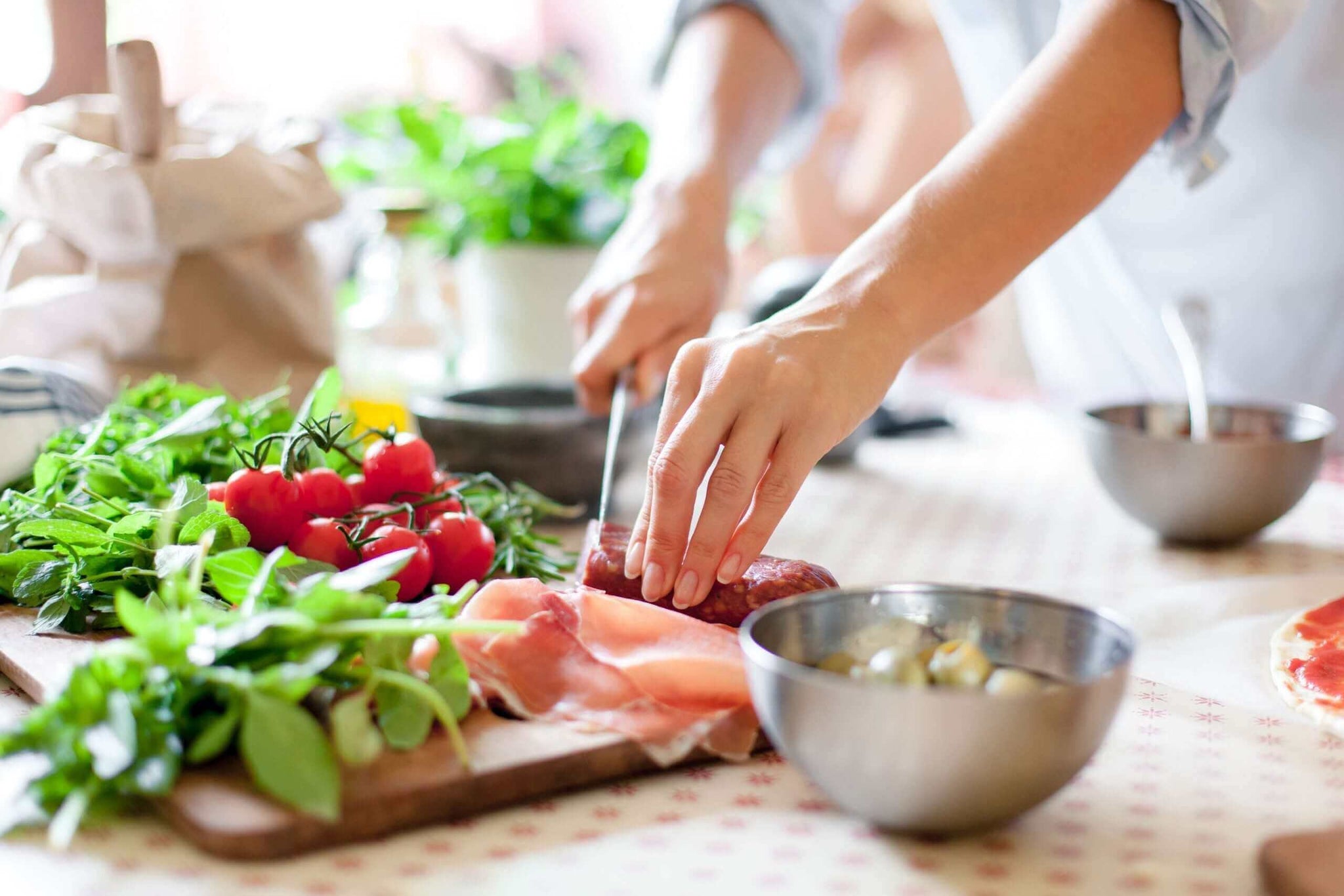 4 recipes A person slicing meat on a cutting board surrounded by various fresh ingredients, including cherry tomatoes, herbs, and leafy greens.