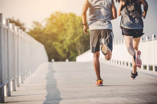 Two people are jogging on a paved path with white railings on both sides.