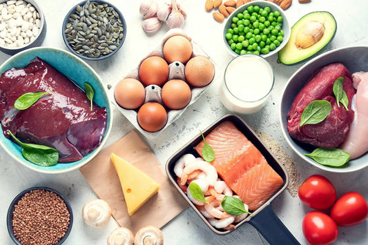 A variety of protein-rich foods are displayed on a light surface, including raw chicken breast,