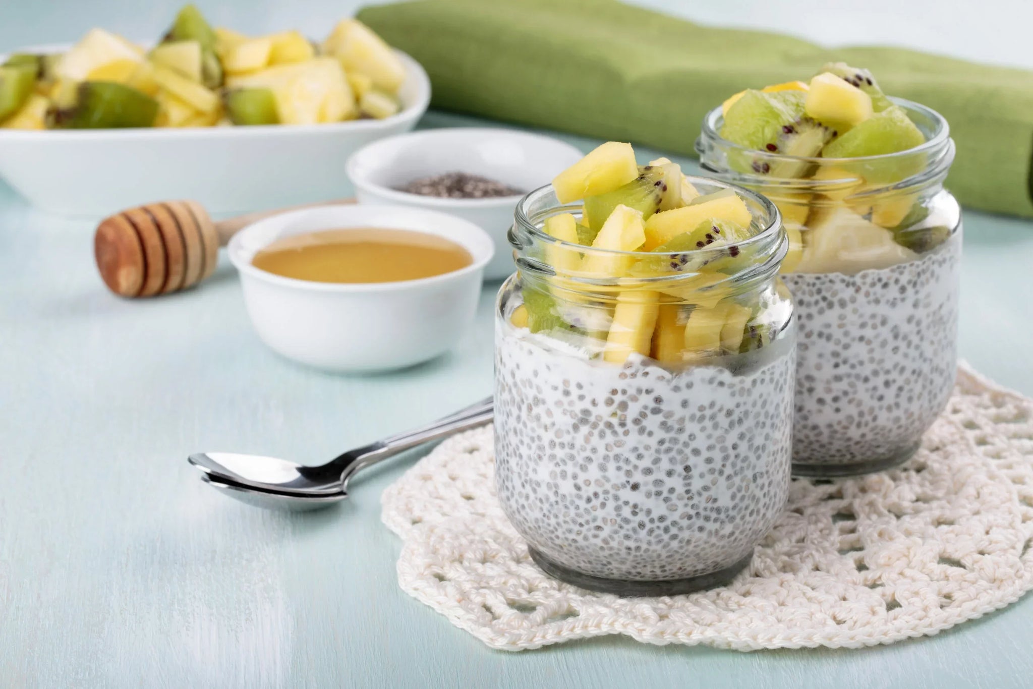 Two glass jars filled with chia pudding, topped with diced kiwi and pineapple pieces.