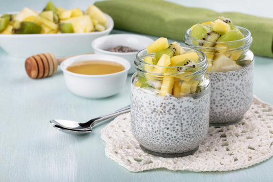 Two glass jars filled with chia pudding, topped with diced kiwi and pineapple pieces.