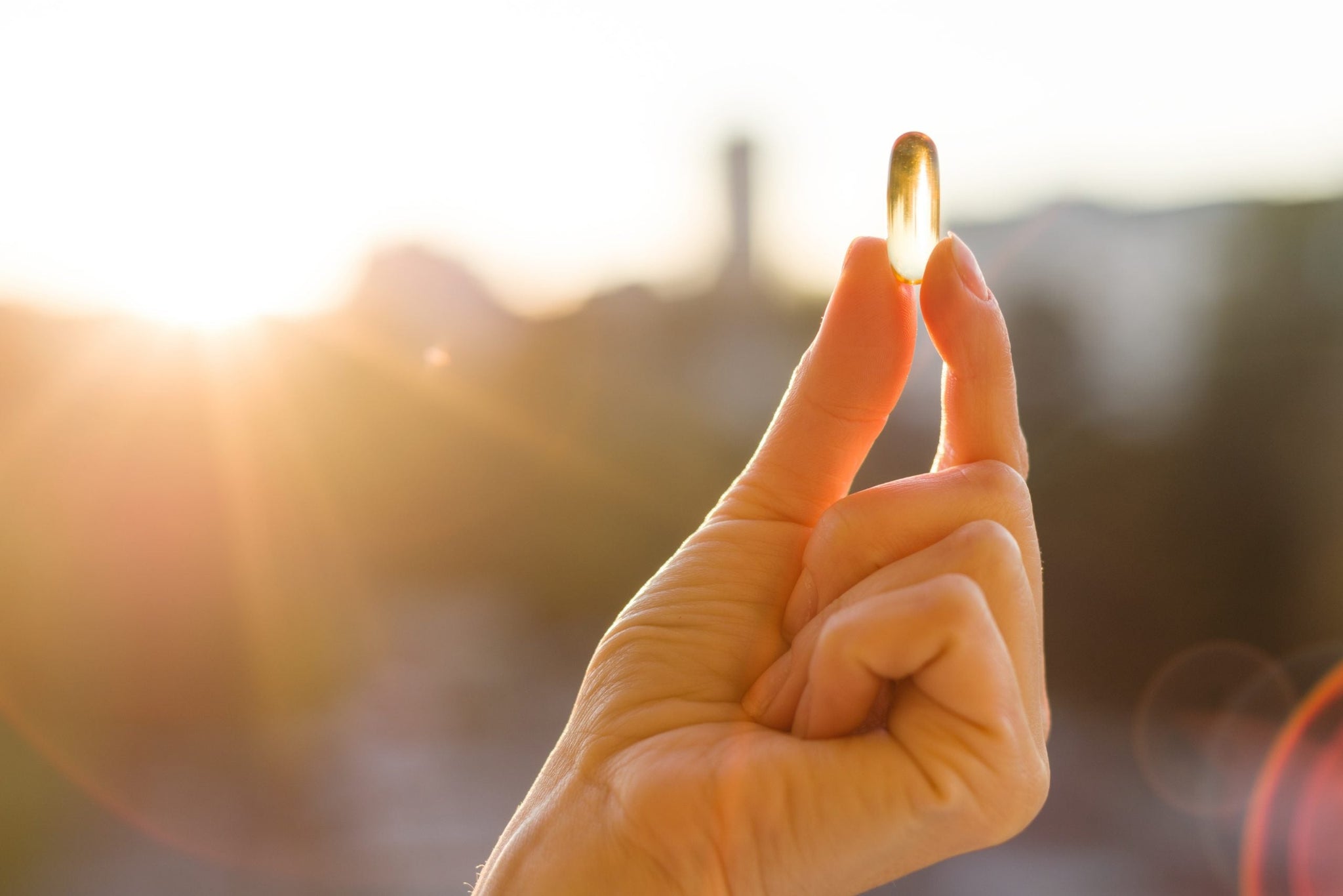 Close-up of a hand holding a transparent yellow capsule between the thumb and index finger