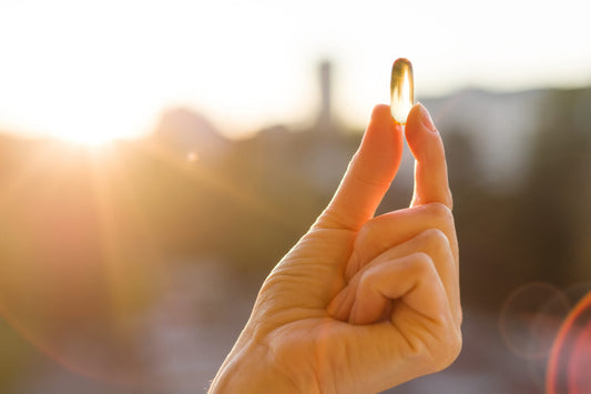 Close-up of a hand holding a transparent yellow capsule between the thumb and index finger