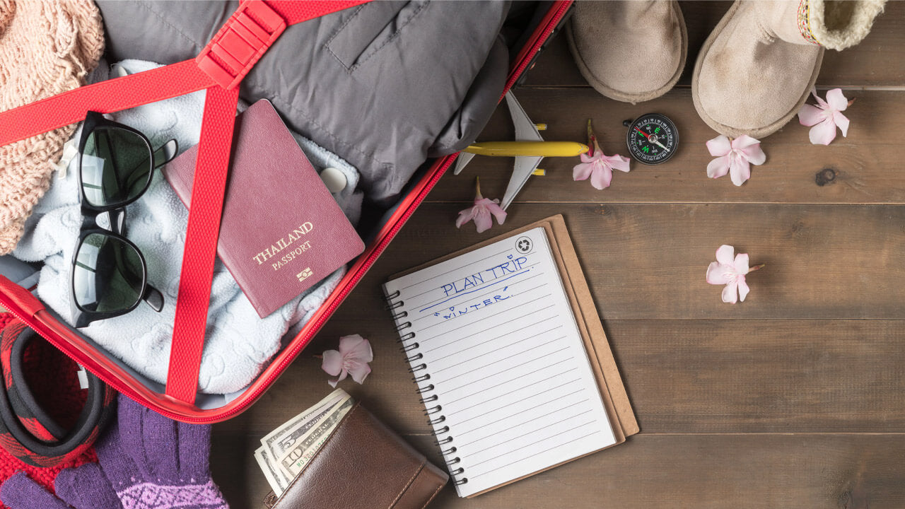 Open red suitcase filled with winter clothes, a passport, sunglasses, and a model airplane lying on the top.