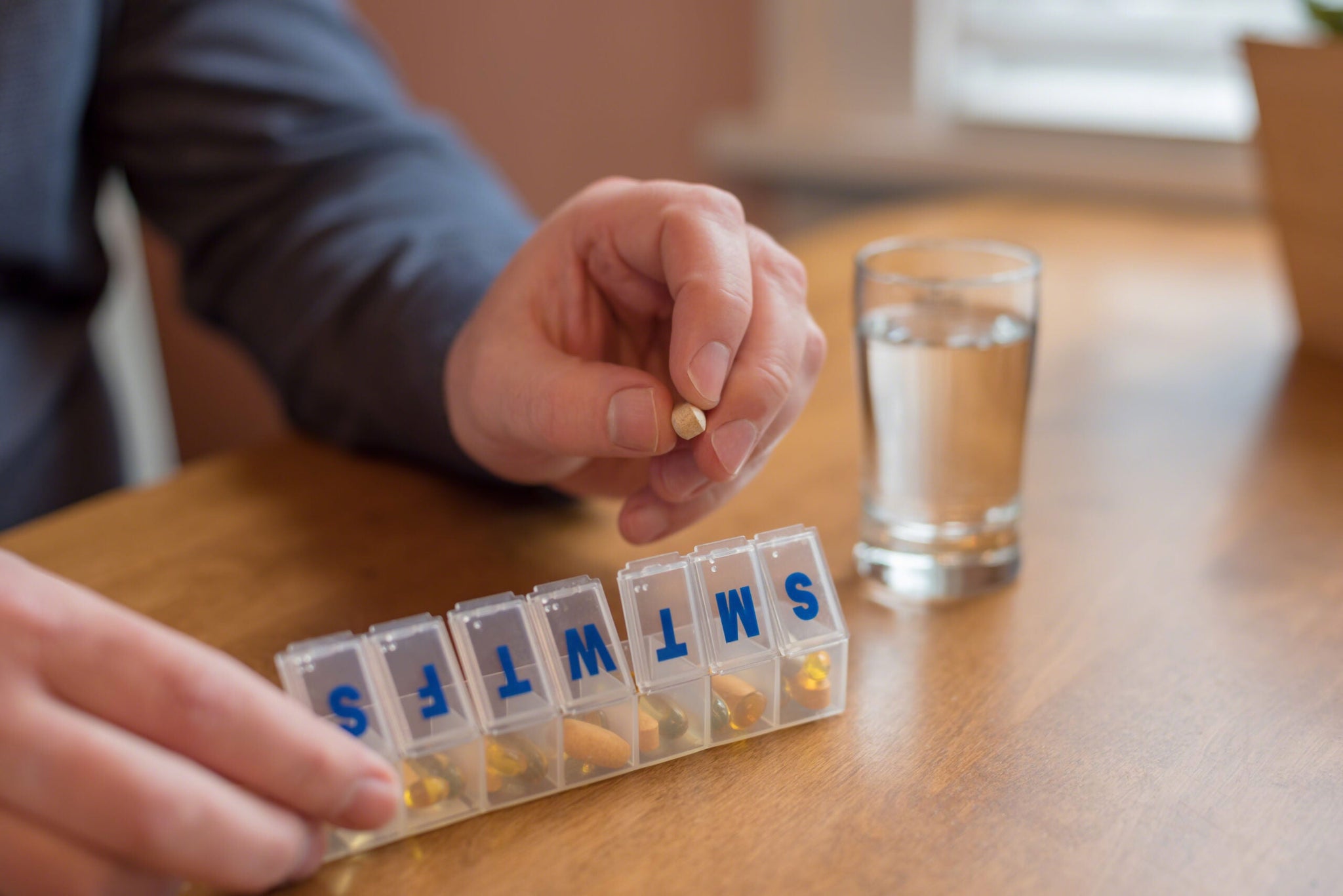 A person is using a weekly pill organizer, labeled with the days of the week, to take medication.