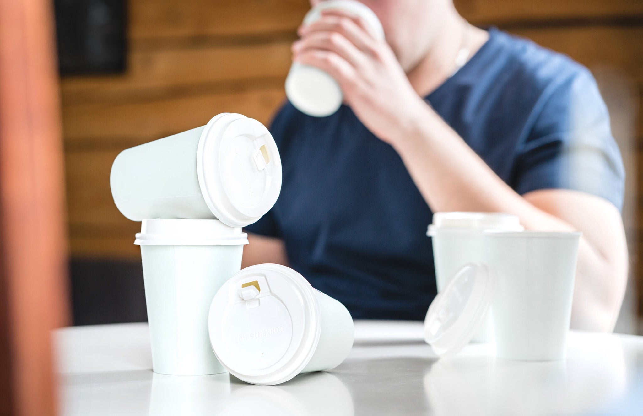 A person in a blue shirt is drinking from a white paper cup with a lid.