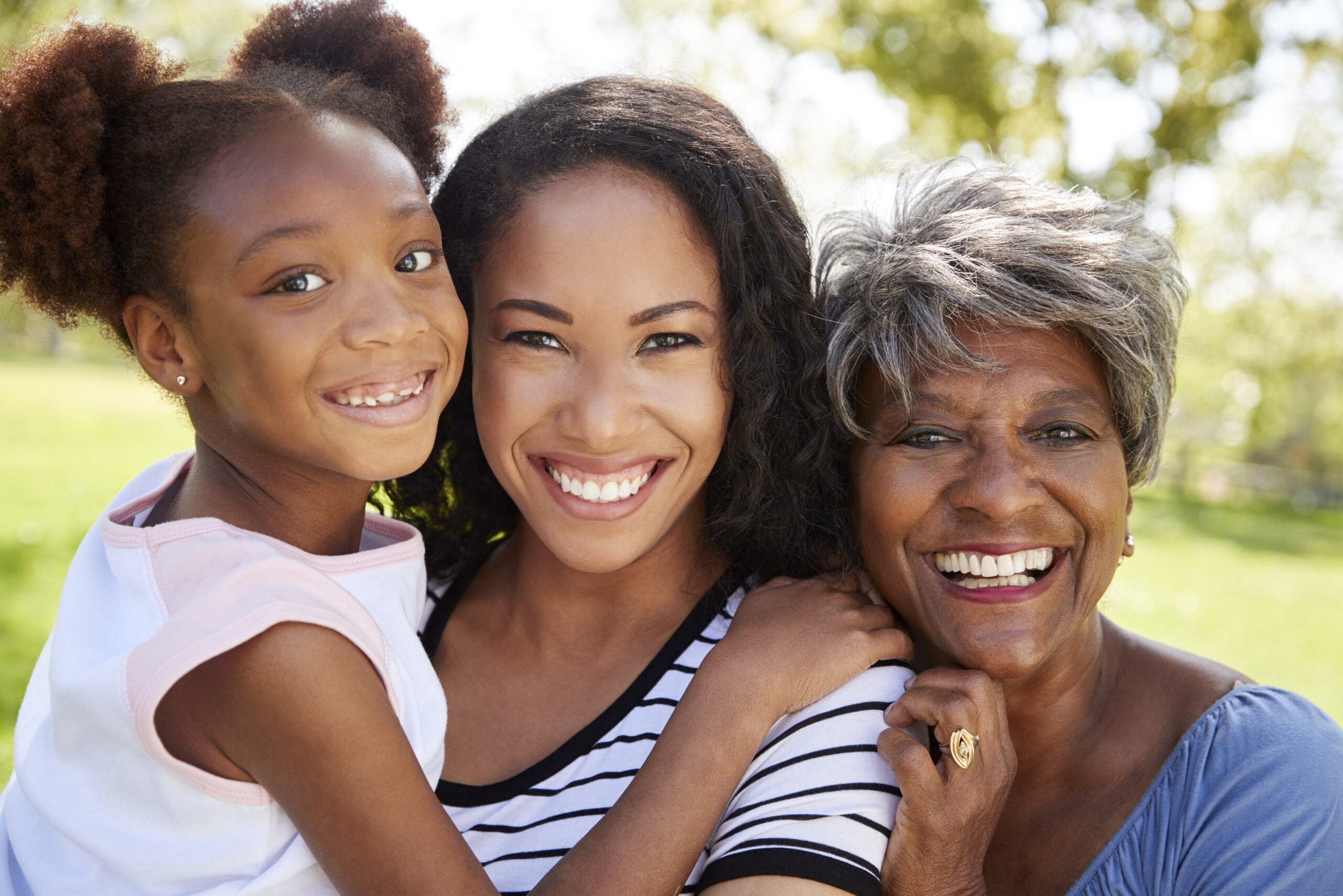 Three generations of women smiling and embracing outdoors.