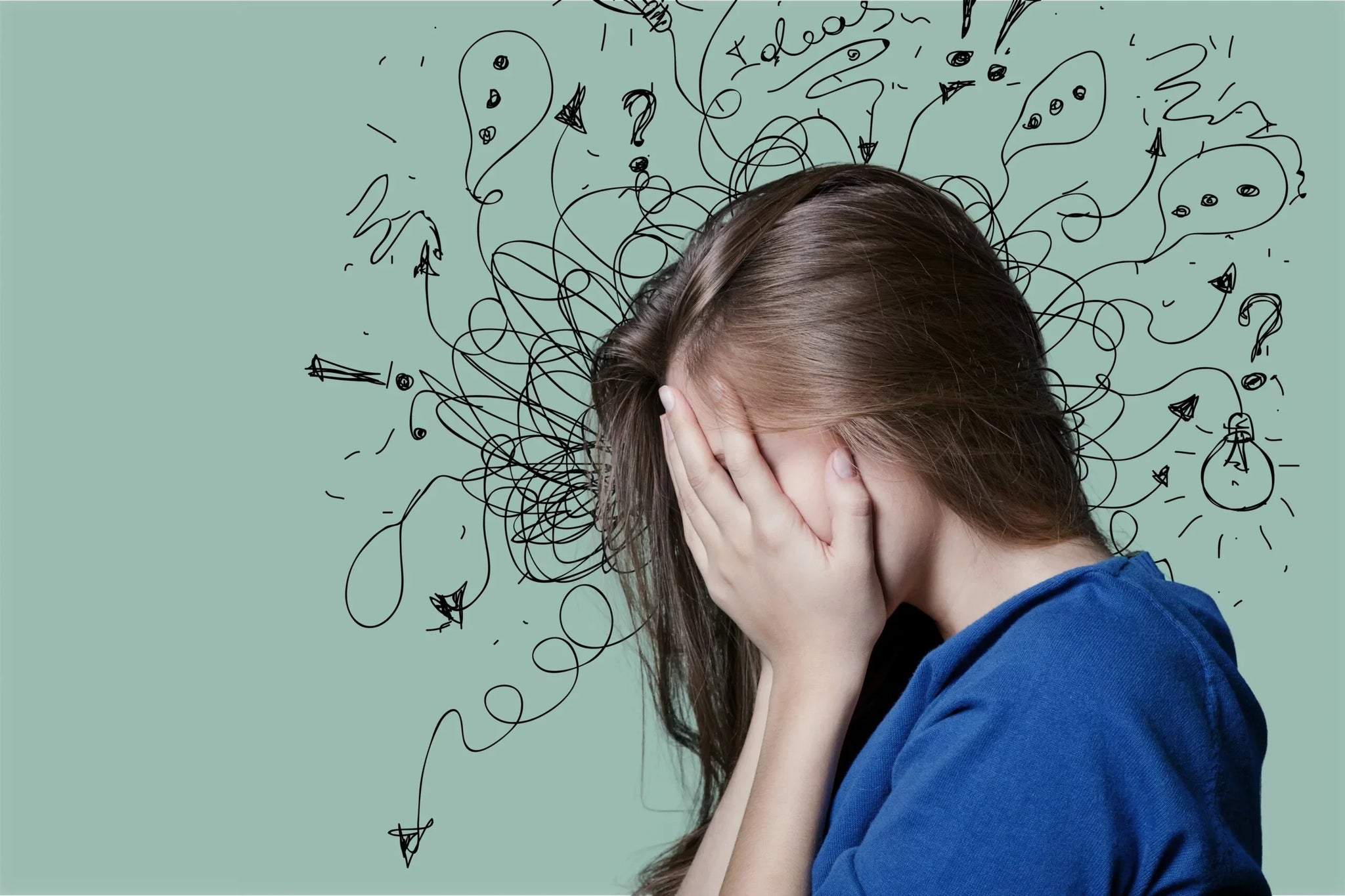 A person with long brown hair wearing a blue shirt covers their face with both hands.