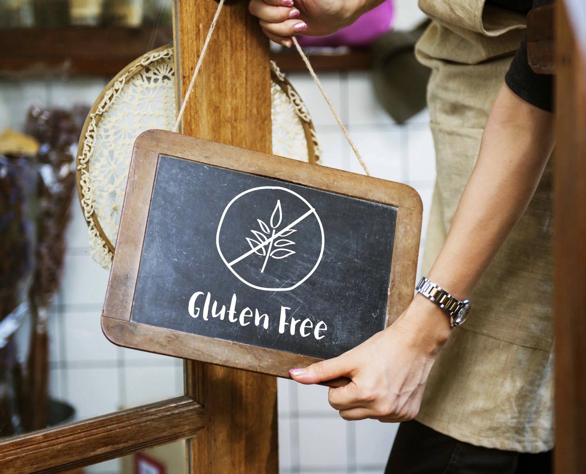 A person wearing an apron is holding a small chalkboard sign hanging on a door.