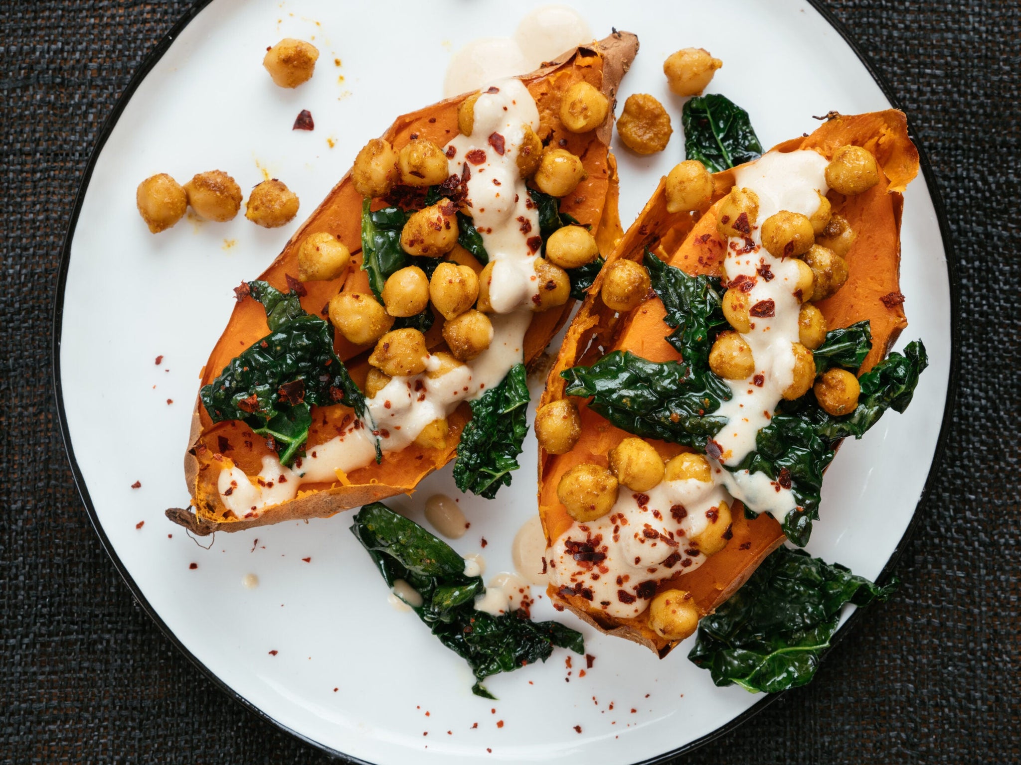 A white plate featuring roasted sweet potato halves topped with crispy chickpeas, sautéed kale, drizzled with a creamy sauce