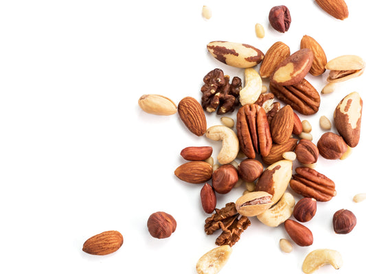 A scattered pile of mixed nuts including almonds, cashews, walnuts, pecans, hazelnuts, and Brazil nuts