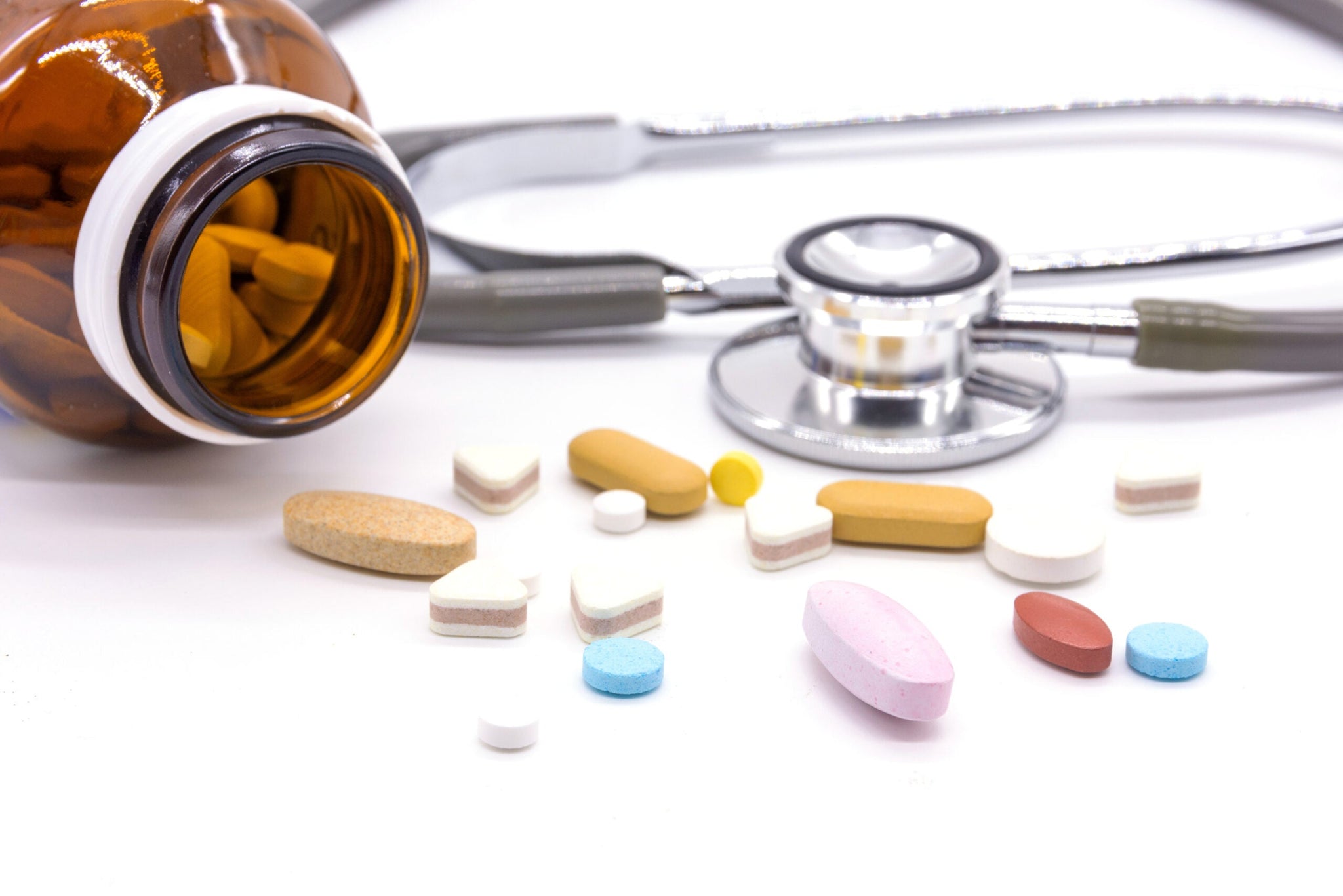 A brown pill bottle is tipped over with variously colored and shaped pills scattered out.
