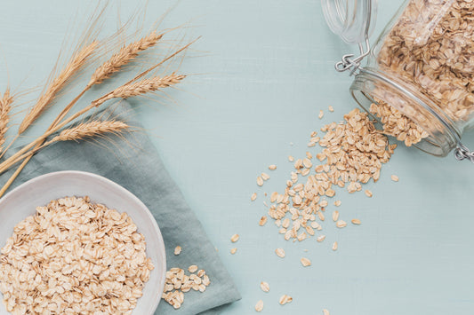 A bowl of oatmeal sits on a light blue surface next to a glass jar with a metal clasp, spilling oats.