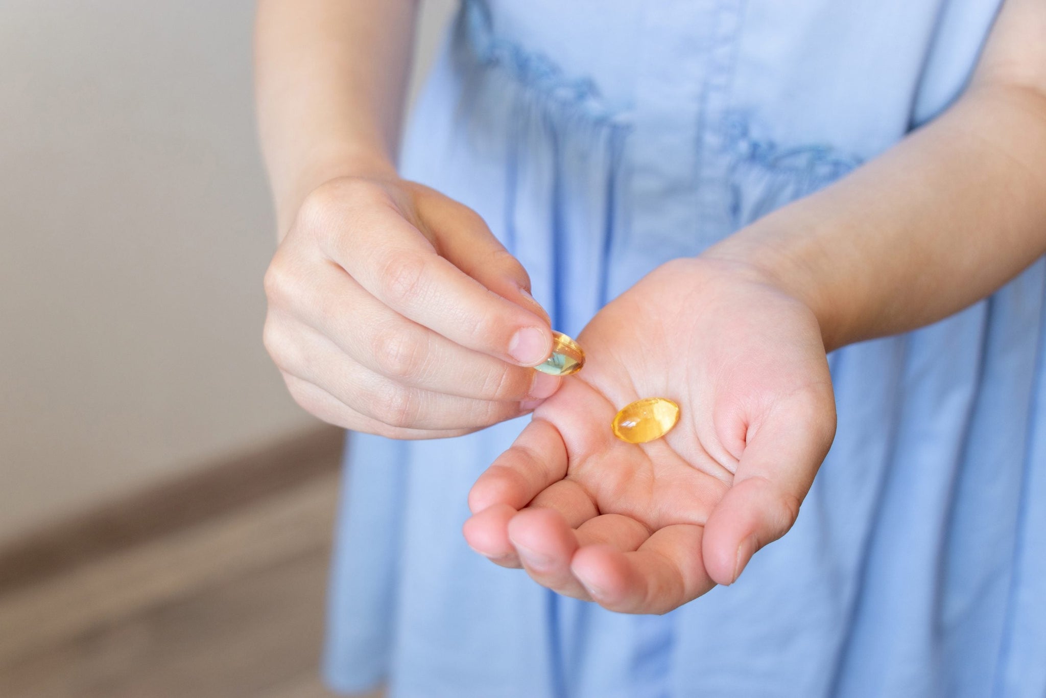 A person in a light blue dress holding a clear goldfish cracker in one hand and another smaller goldfish cracker in the other hand.